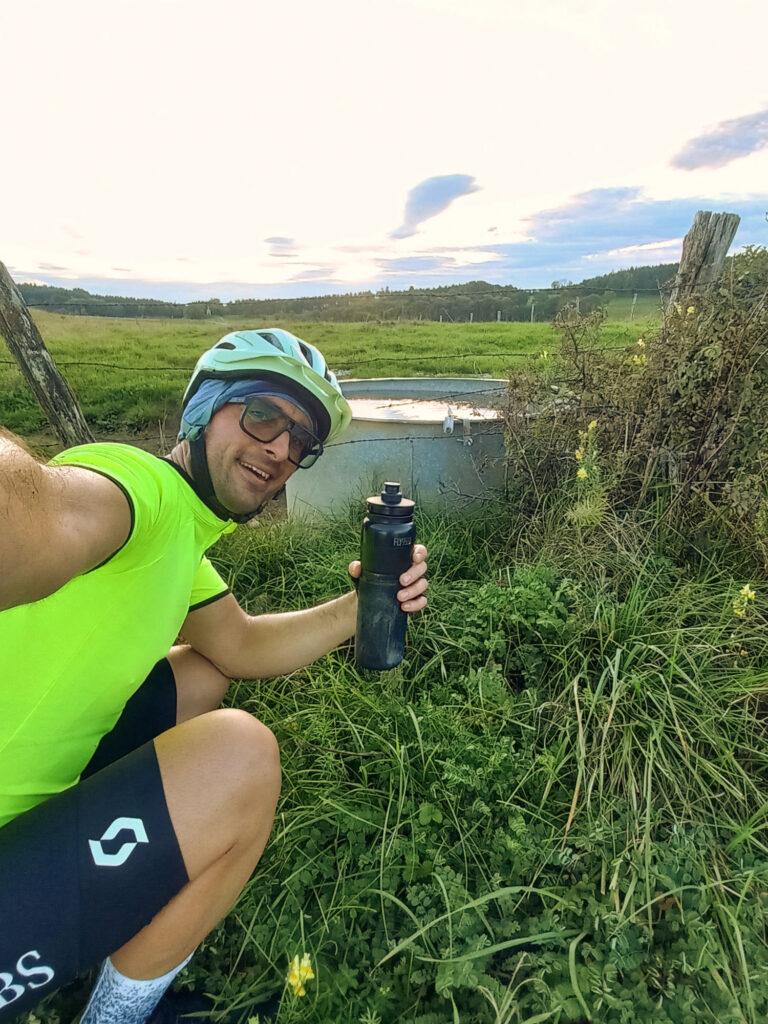 cycling selfie before refilling a water bottle beside a livestock water tank in rural France