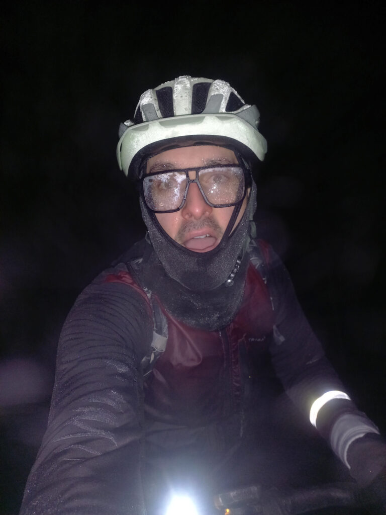 Cyclist covered in frost during a freezing winter night ride, with icy glasses, helmet, balaclava and frozen clothing