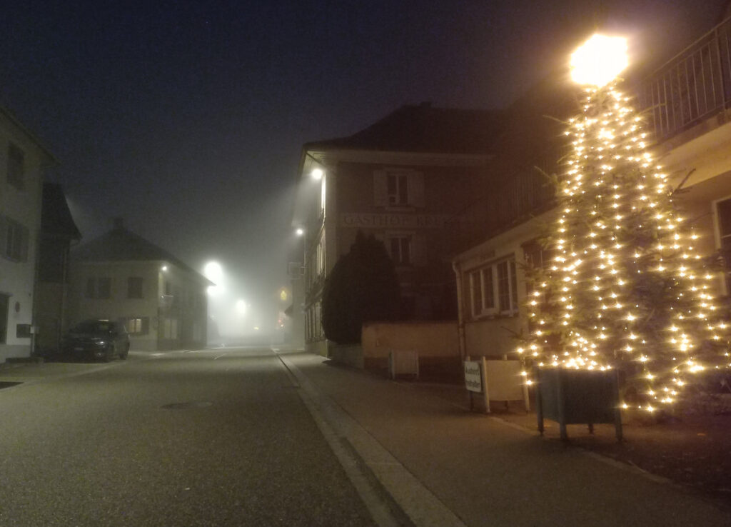 Foggy winter street with a glowing Christmas tree during a cold night cycling ride in Switzerland