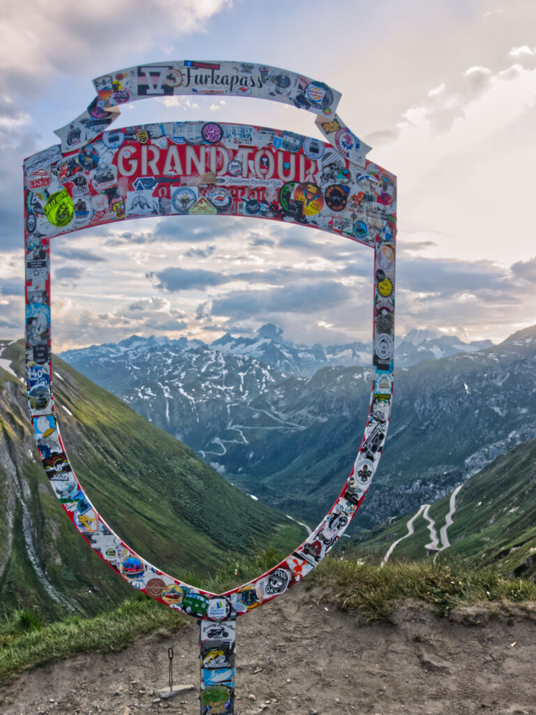 Grand Tour shield framing the serpentine roads of Furka and Grimsel passes.