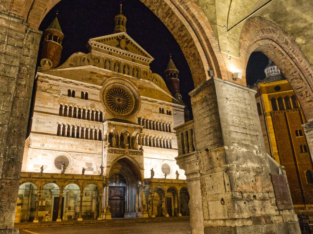 Nočný pohľad spod arkád Palazzo Comunale na osvetlenú katedrálu Santa Maria Assunta v Cremone